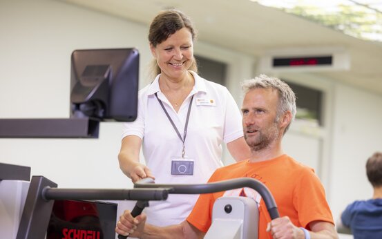 Physiotherapeutin unterstützt männlichen Patienten beim Krafttraining an Trainingsgerät