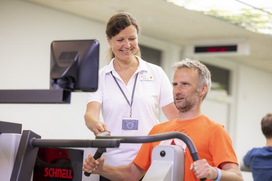 Physiotherapeutin unterstützt männlichen Patienten beim Krafttraining an Trainingsgerät