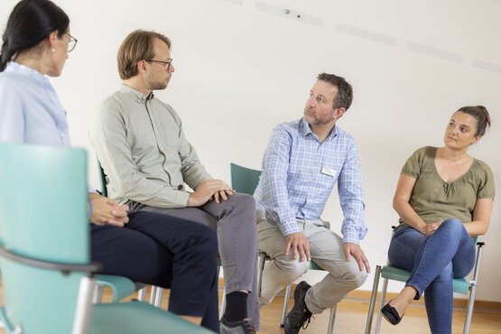 Vier Erwachsene sitzen in hellem Raum im Stuhlkreis und führen Gespräch, Teamarbeit und Vielfalt