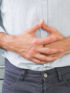 Mann in hellblauem Hemd hält sich den Bauch mit beiden Händen