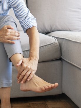 Person sitzt auf einem Sofa und massiert schmerzendes Bein