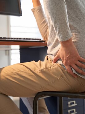 Person sitzt am Schreibtisch und hält sich mit Schmerzen die Hüfte