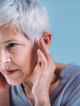 Ältere Person hält sich das Ohr vor Schmerzen