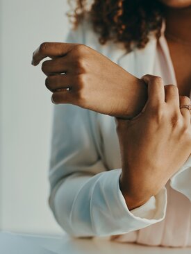 Frau in weißer Bluse hält sich ihr schmerzendes Handgelenk