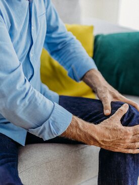 Mann sitzt auf dem Sofa und hält sich das rechte Knie bei Knieschmerzen