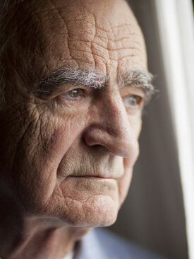 Älterer Mann schaut nachdenklich aus dem Fenster