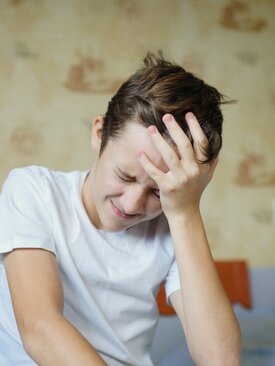 Junge hält sich den Kopf vor Schmerzen, Symbolbild für Kopfschmerzen bei Kindern