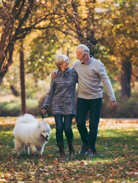 Älteres Paar spaziert mit großem weißen Hund im herbstlichen Park