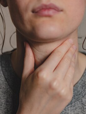 Frau tastet ihren Hals wegen Schilddrüsenvergrößerung, Symbolbild Stoffwechselerkrankung