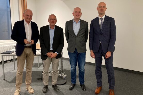 Vier männliche Referenten in Businesskleidung stehen nebeneinander in modernem Veranstaltungsraum mit Technik – medizinisches Symposium