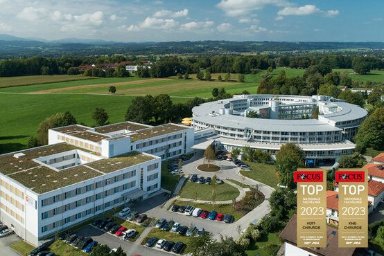 Luftaufnahme mit weißem, ringförmigem Gebäude im Grünen; im Vordergrund zwei Focus-Siegel für Top-Klinik Hüft- und Kniechirurgie 2023