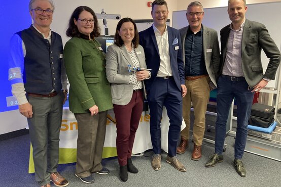 Sechs Geschäftspersonen, drei Frauen und drei Männer, stehen nebeneinander in einem Konferenzraum