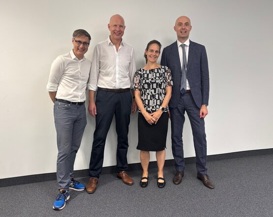 Vier Referenten, drei Männer und eine Frau, stehen lächelnd nebeneinander vor weißer Wand beim 6. Intensivsymposium