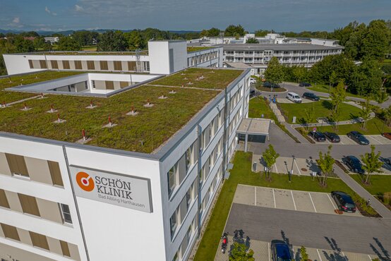 Luftaufnahme der Schön Klinik Bad Aibling Harthausen mit begrüntem Flachdach, Parkplatz, Grünflächen und umliegender Landschaft