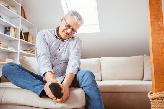 Mann sitzt auf der Couch und hält sich den Fuß