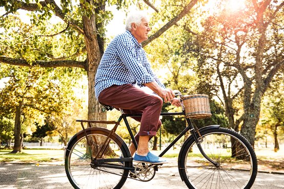 Älterer Mann fährt bei Sonnenschein auf klassischem Fahrrad durch grünen Park mit Bäumen