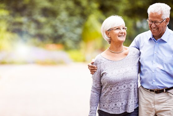 Glückliches älteres Paar spaziert gemeinsam im Park, beide Senioren tragen Brillen und lächeln