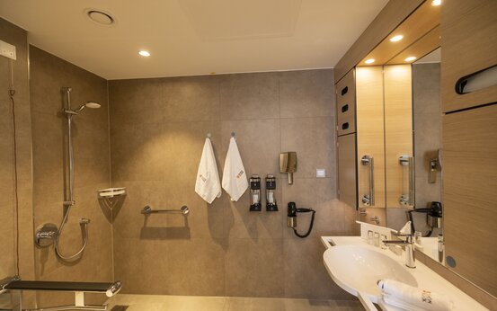 Modernes, barrierefreies Klinik-Badezimmer mit bodengleicher Dusche, Haltegriffen, Duschsitz und unterfahrbarem Waschbecken