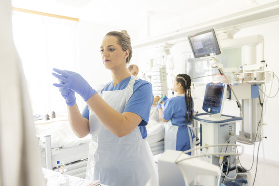 Pflegekraft bereitet Spritze auf Intensivstation vor, zwei weitere betreuen Patienten, Überwachungsmonitore und Medizintechnik im Hintergrund