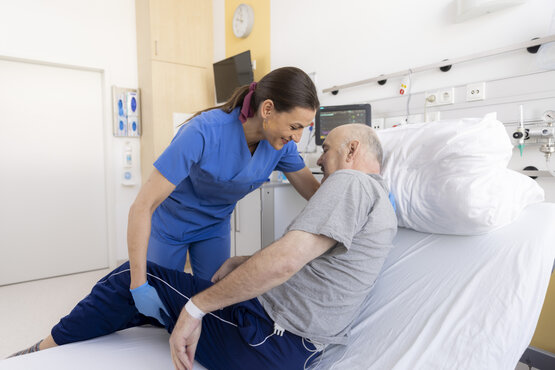 Krankenschwester in blauer Kleidung hilft älterem Patienten beim Aufrichten aus dem Bett