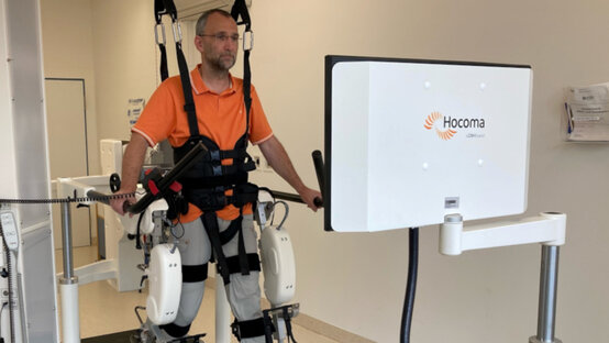 Mann mit Brille im orangefarbenen Poloshirt trainiert im Exoskelett am robotergestützten Gangtherapie-System Lokomat