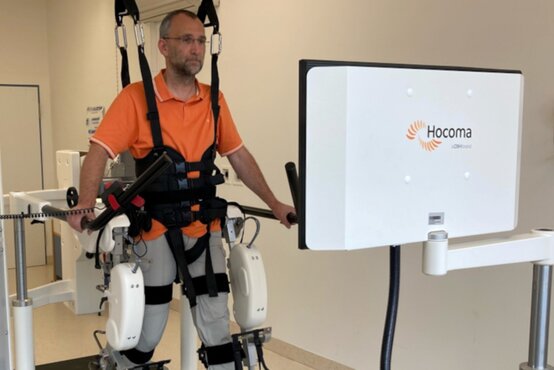 Mann mit Brille im orangefarbenen Poloshirt trainiert im Exoskelett am robotergestützten Gangtherapie-System Lokomat