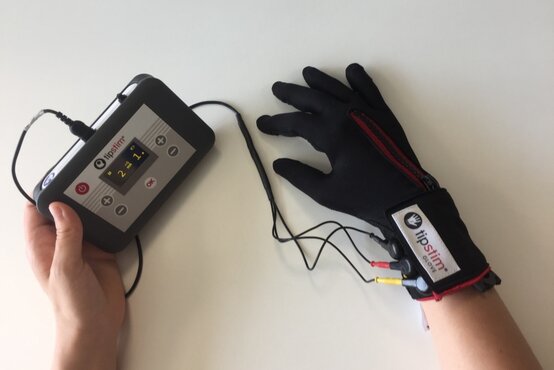 Person hält medizinisches Gerät mit Display, trägt tipstim® GLOVE mit Kabeln