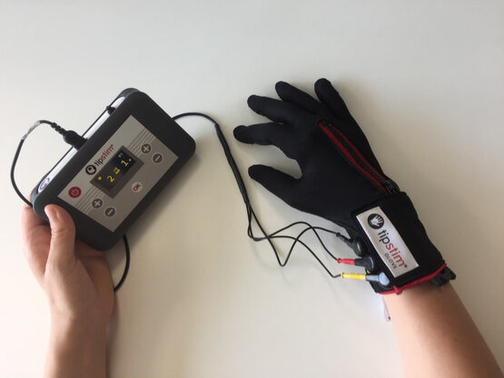 Person hält medizinisches Gerät mit Display, trägt tipstim® GLOVE mit Kabeln