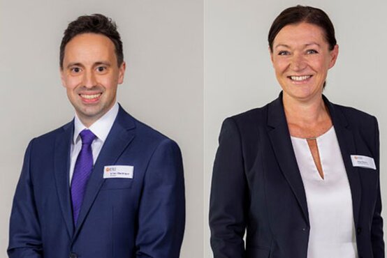 Zwei Mitglieder der Klinik-Geschäftsführung stehen nebeneinander in Businesskleidung mit Namensschildern