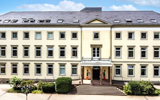 Dreistöckiges klassizistisches Herrenhaus mit gelber Fassade, breiter Steintreppe, Säulen und gepflegtem Vorgarten