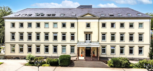 Dreistöckiges klassizistisches Herrenhaus mit gelber Fassade, breiter Steintreppe, Säulen und gepflegtem Vorgarten