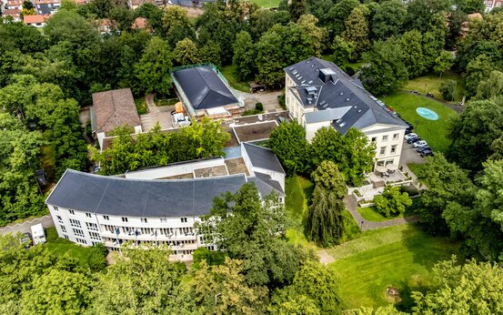 Luftaufnahme der Schön Klinik Bad Arolsen mit modernen und historischen Bauten in grüner Parkanlage, halbkreisförmiges Gebäude im Vordergrund
