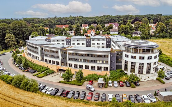 Luftaufnahme der Schön Klinik Bad Arolsen mit gebogener Fassade, Parkplatz, Bäumen und viel Grün