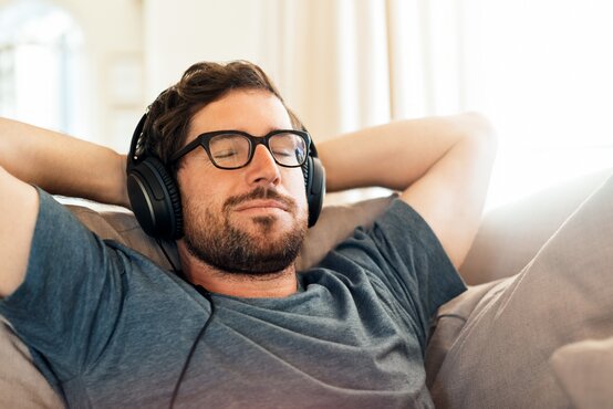 Mann entspannt auf Sofa mit Kopfhörern und genießt beschwerdefreies Hören nach Hörbehandlung