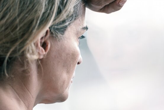 Nachdenkliche Frau mit blonden Haaren lehnt Stirn an Fenster, besorgt, Spiegelung im Glas