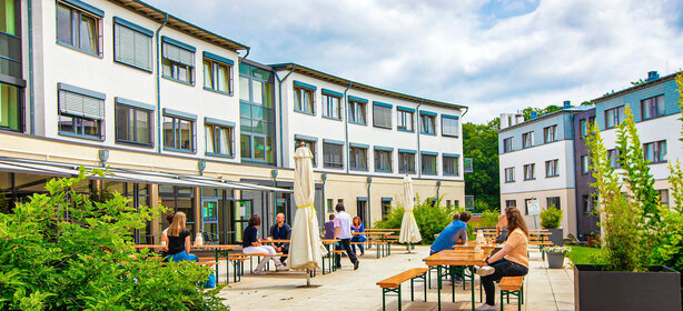 Menschen sitzen entspannt an Holzbänken im begrünten Innenhof