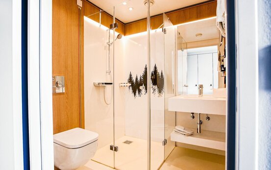 Modernes, helles Badezimmer mit Holzverkleidung, bodenebener Dusche mit Tannenwald-Motiv, wandhängendem WC und großem Spiegel