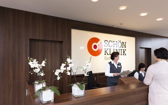 Empfangsbereich der Schön Klinik Bad Arolsen mit dunklem Holz, Orchideen, beleuchtetem Logo