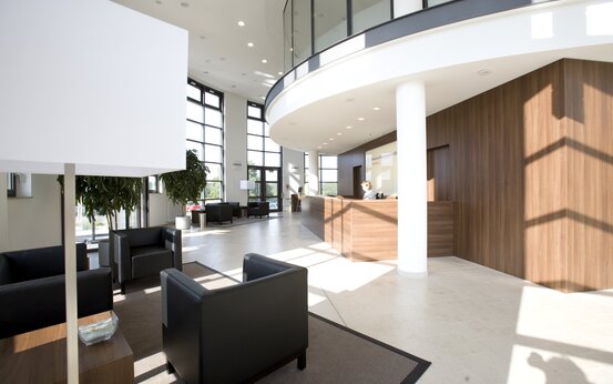 Heller, moderner Empfangsbereich mit großer Fensterfront, hölzerner Empfangstheke, Ledersesseln, Pflanzen und Galerie im Obergeschoss