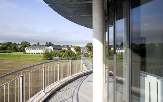 Blick von modernem, überdachtem Balkon mit Geländer auf begrüntes Gelände