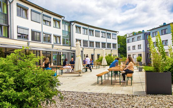 Menschen sitzen entspannt an Holzbänken im begrünten Innenhof