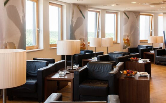 Helle, moderne Klinik-Lounge mit schwarzen Ledersesseln, großen Fenstern und Beistelltischen