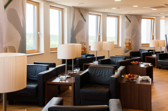 Helle, moderne Klinik-Lounge mit schwarzen Ledersesseln, großen Fenstern und Beistelltischen