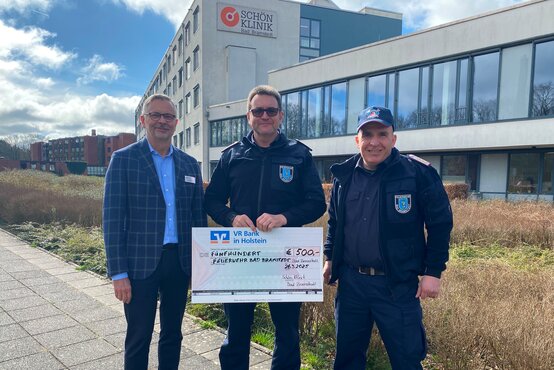 Drei Männer vor der Schön Klinik Bad Bramstedt halten symbolischen Spendenscheck der VR Bank Holstein
