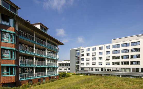 Zwei moderne Klinikgebäude mit großen Fenstern, gepflegte Grünfläche, sonniges Wetter, blauer Himmel