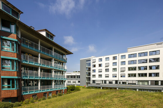 Zwei moderne Klinikgebäude mit großen Fenstern, gepflegte Grünfläche, sonniges Wetter, blauer Himmel