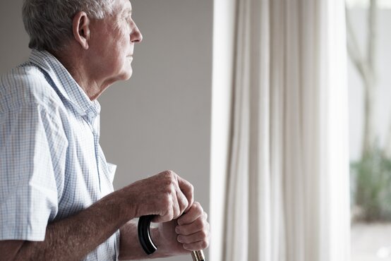 Älterer Mann mit Gehstock blickt nachdenklich aus dem Fenster