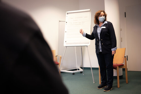 Frau mit Maske hält Vortrag vor Flipchart im modernen Seminarraum