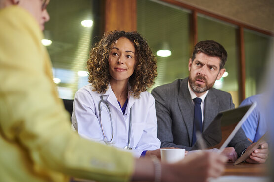 Ärztin mit Stethoskop und Team aus verschiedenen Berufsgruppen im Gespräch am Konferenztisch im Büro