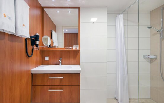 Badezimmer mit bodengleicher Dusche, rutschfesten Fliesen, modernem Waschbecken und beleuchtetem Spiegel